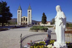 madonna di medjugorje con chiesa alle spalle